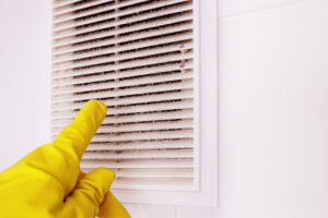 Homeowner wearing yellow cleaning gloves points to built up dust on vent cover.